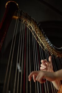 Vertical shot of female hands plucking harp strings professionally playing enchanting music on stage in philharmonic hall